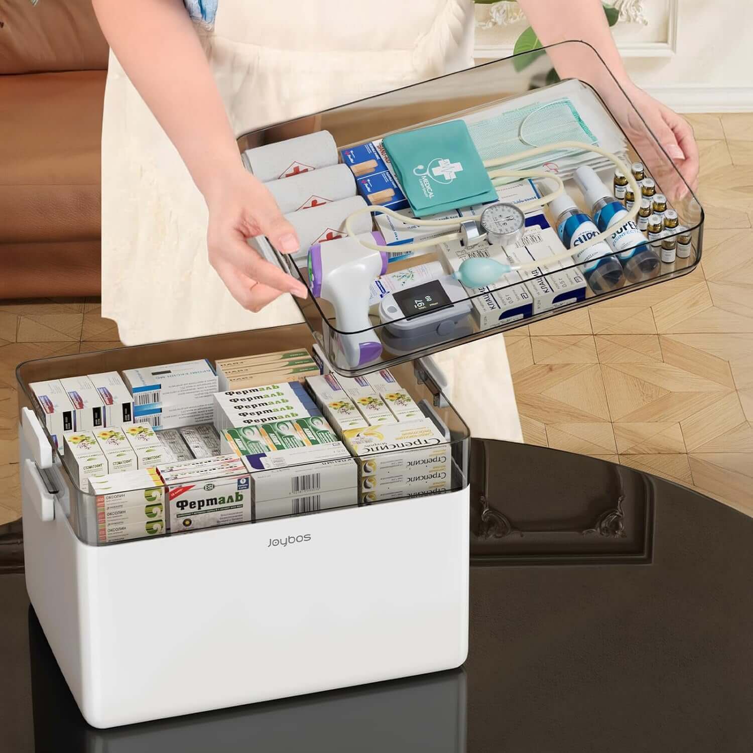 Person handling a multi-tiered medical box filled with medications, featuring compartments for organized storage and a soft leather handle.
