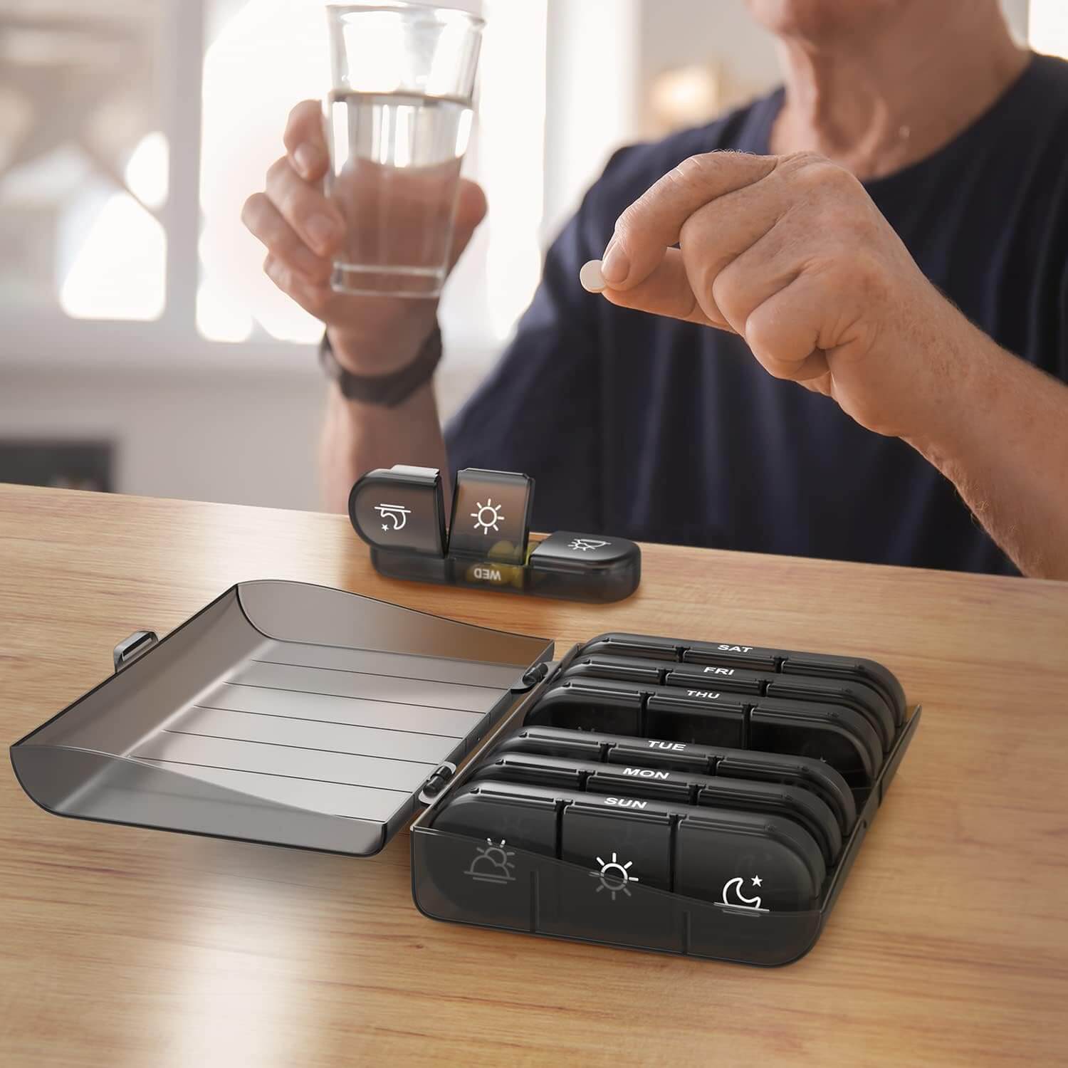 Medivita 7-Day Pill Organizer with large compartments for medication, shown on a table with a person holding a tablet and water.